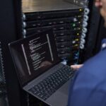 Technicien debout devant le serveur Rack tenant un ordinateur portable avec un code d'affichage ouvert terminal.